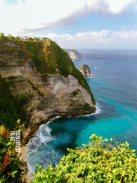 Turquoise sea against tall cliffs under bright sun.