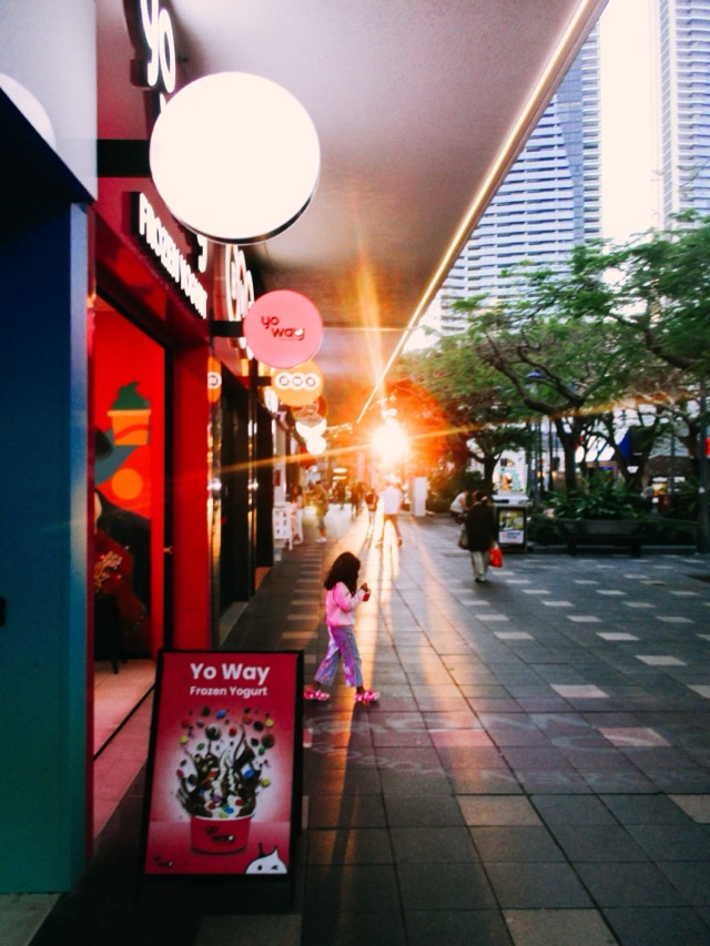 A child walking past a frozen yogurt shop as the sun flares down the street.